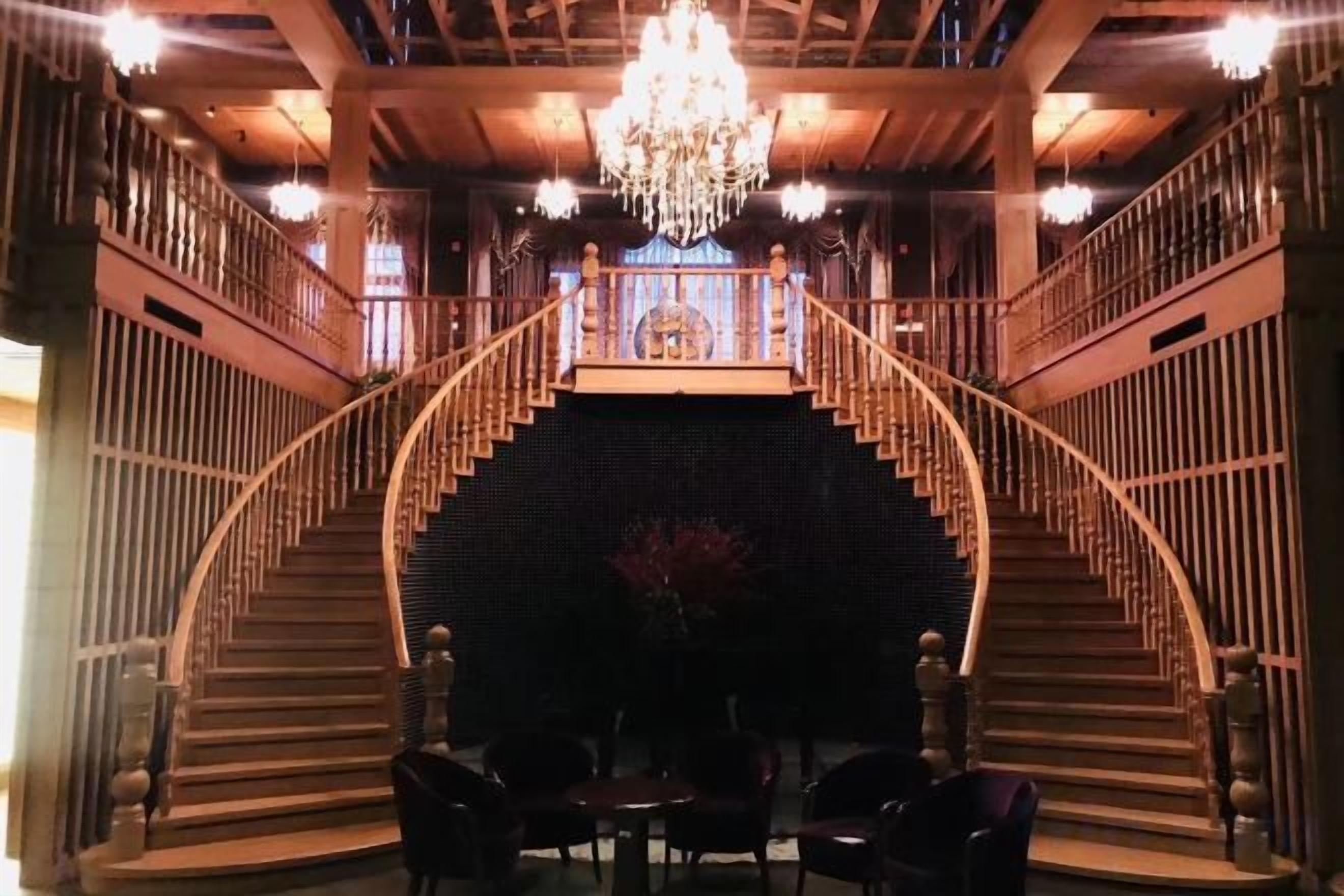 A grand staircase with a chandelier, leading to a balcony.