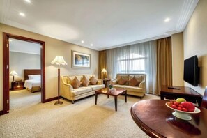 A hotel room with a bed, a sofa, a coffee table, a TV, and a dining table with fruit. - Shanghai Pudong Lingang Kaiyuan Hotel (Shanghai)