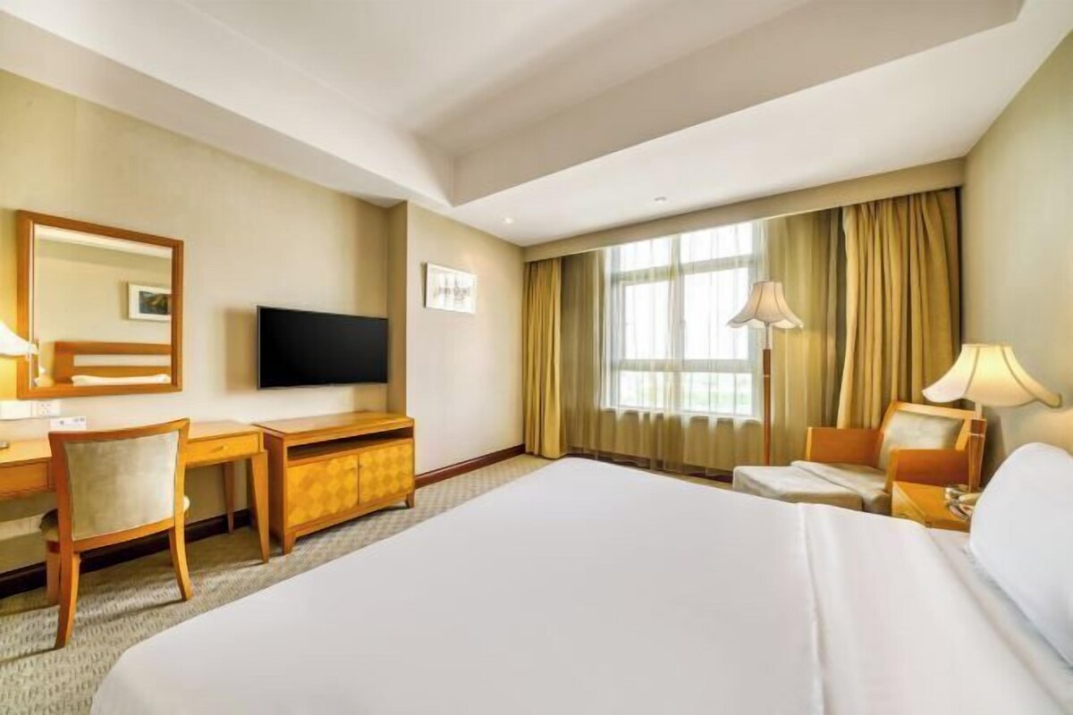A hotel room with a large bed, a desk with a chair, a television, and a window with curtains.
