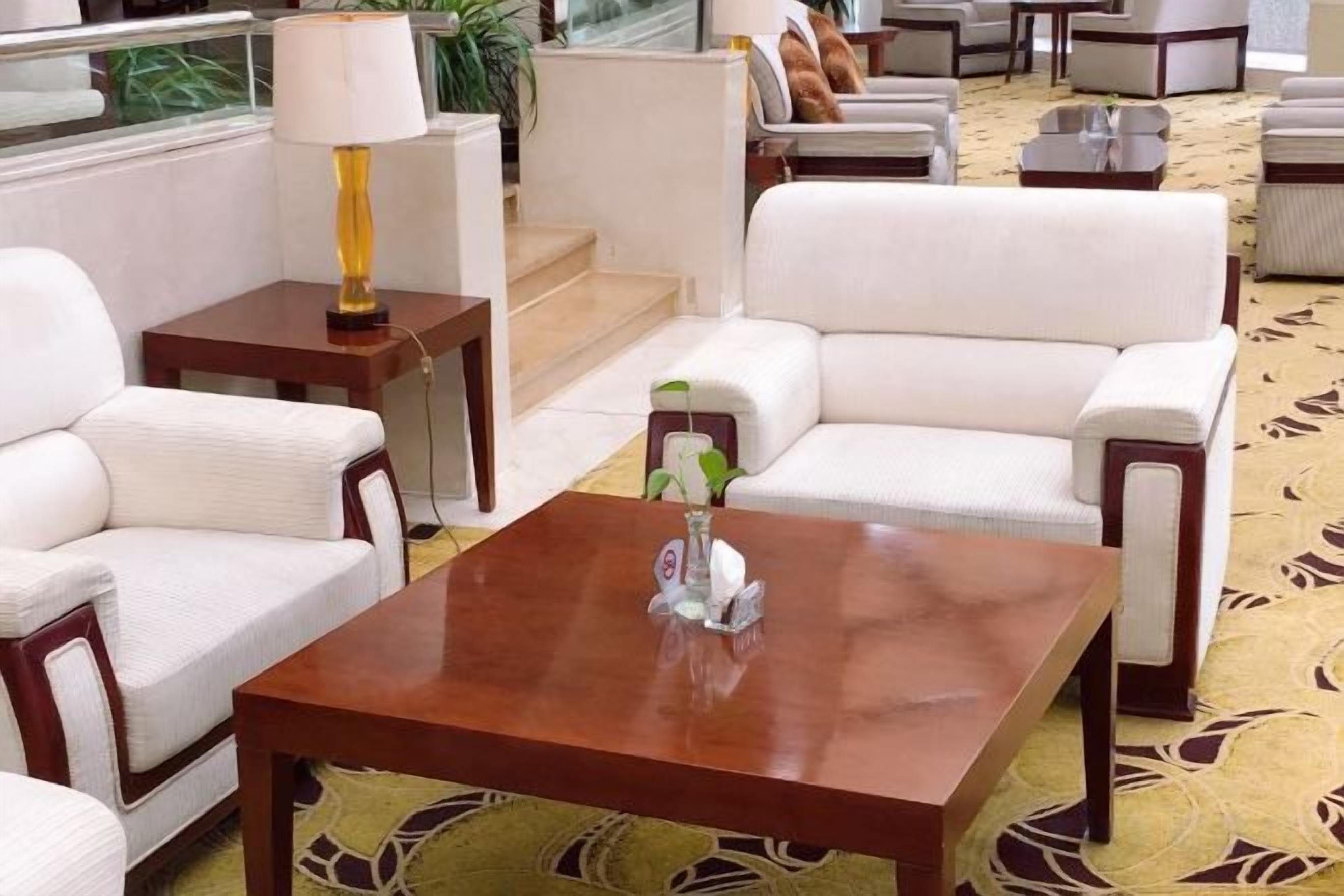 A hotel lobby with a seating area featuring a sofa and armchairs, a coffee table with a vase, and a lamp on a side table.