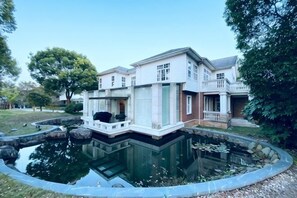 A two-story house with a pond in front, a covered porch, and a well-maintained lawn. - Shanghai Pudong Lingang Kaiyuan Hotel (Shanghai)