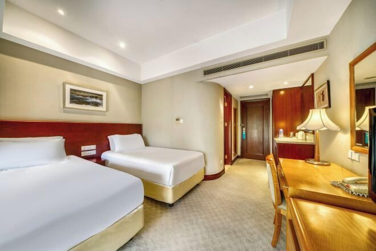 A hotel room with two beds, a wooden desk, a chair, a lamp, and a mirror.