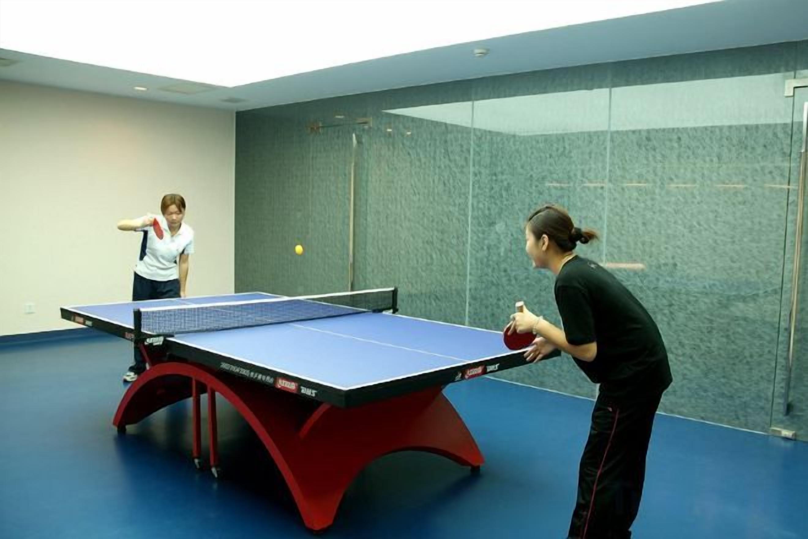 Una mesa de ping pong en una habitación con un separador de vidrio y piso azul.