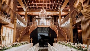 Un salón imponente con una escalera central, una araña y arreglos florales.