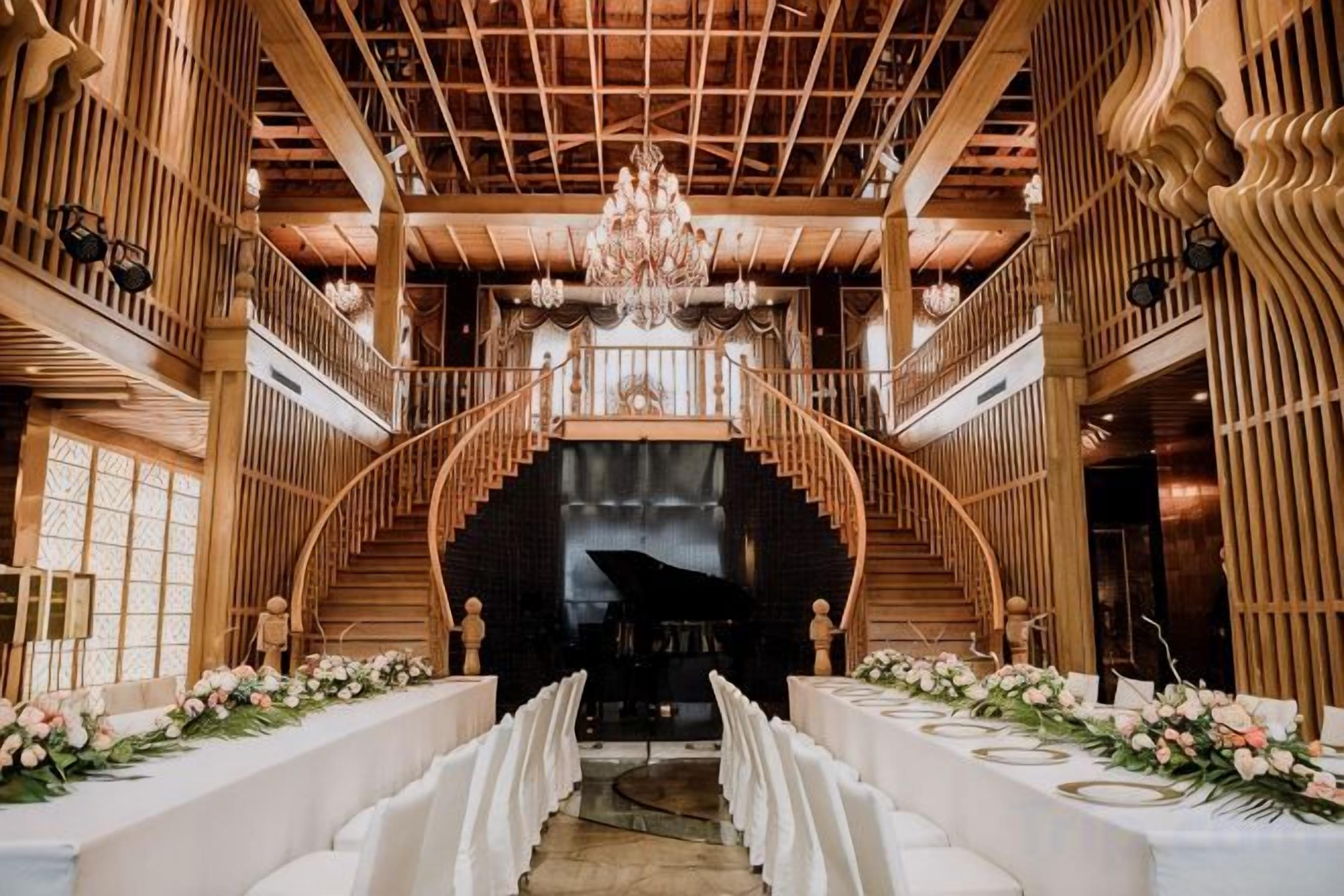 Un salón imponente con una escalera central, un candelabro y un piano.