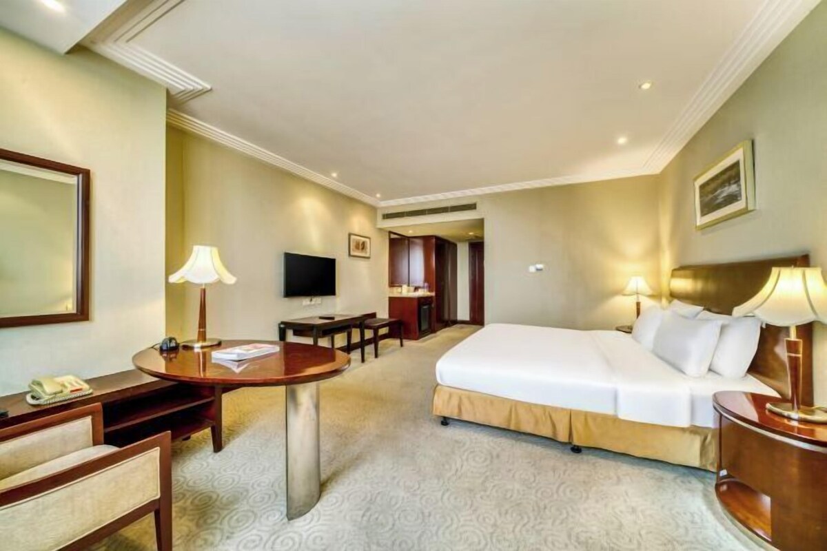 A hotel room with a bed, a desk, a chair, a TV, and a lamp.