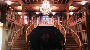 Una imponente escalera con candelabro, barandillas de madera y una pared de azulejos oscuros en la parte inferior.