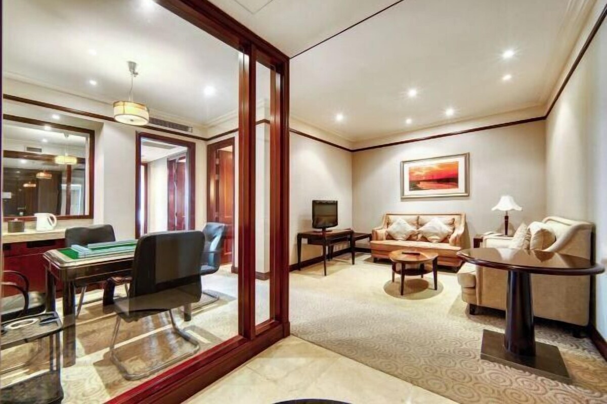 A hotel room with a dining area, a sofa set, a television, and a painting on the wall.