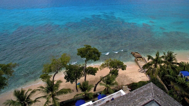 Vista de una playa con aguas turquesas cristalinas, palmeras y una orilla arenosa.