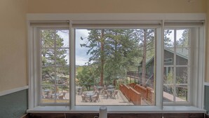 Une pièce dotée d’une grande fenêtre donnant sur une terrasse extérieure aménagée avec des tables et des chaises.