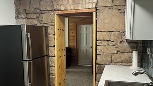 A kitchen with a stone wall, a refrigerator, a sink, and a wooden door leading to another room. - My Blue Haven is a Walkers Paradise 5 min to the Monument and 15 min to Downtown (Rapid City)