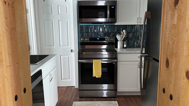 A compact kitchen with white cabinets, stainless steel appliances, and a teal accent wall. - My Blue Haven is a Walkers Paradise 5 min to the Monument and 15 min to Downtown (Rapid City)