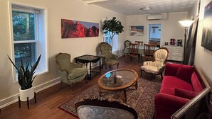 A living room with a red sofa, two armchairs, a coffee table, and a patterned rug. There is a potted plant and a painting on the wall. - My Blue Haven is a Walkers Paradise 5 min to the Monument and 15 min to Downtown (Rapid City)
