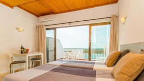 Ett hotellrum med en säng, ett litet skrivbord och en balkong med utsikt över havet.