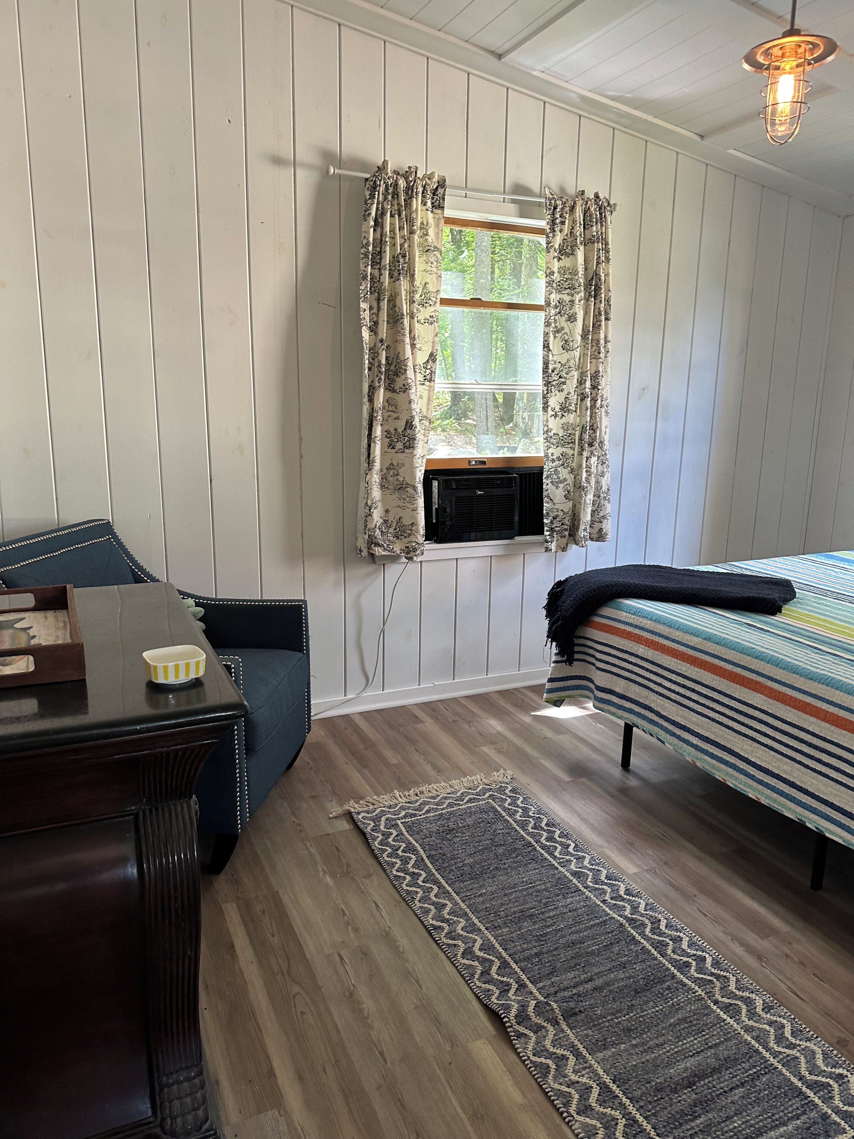 Una habitación con cama, escritorio, ventana con cortinas, radiador y alfombra.