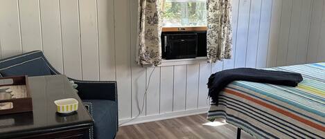 Una habitación con cama, escritorio, ventana con cortinas, radiador y alfombra.