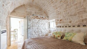 A bedroom with a stone wall, a bed with a patterned bedspread, and a wooden hanger rack.