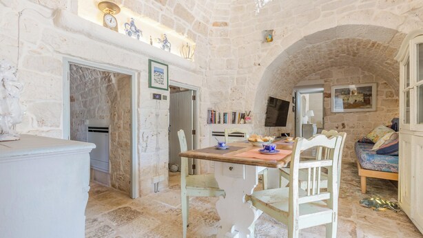 A stone-walled room with a dining table, chairs, a bed, and a television.