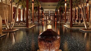 A luxurious lobby with a central water feature, palm trees, and seating areas.