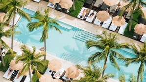 A large pool with multiple sun loungers and palm trees.