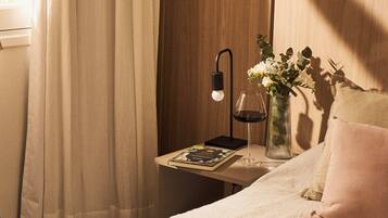 A bedroom with a bed, a bedside table with a lamp, a vase with flowers, and a window with curtains.