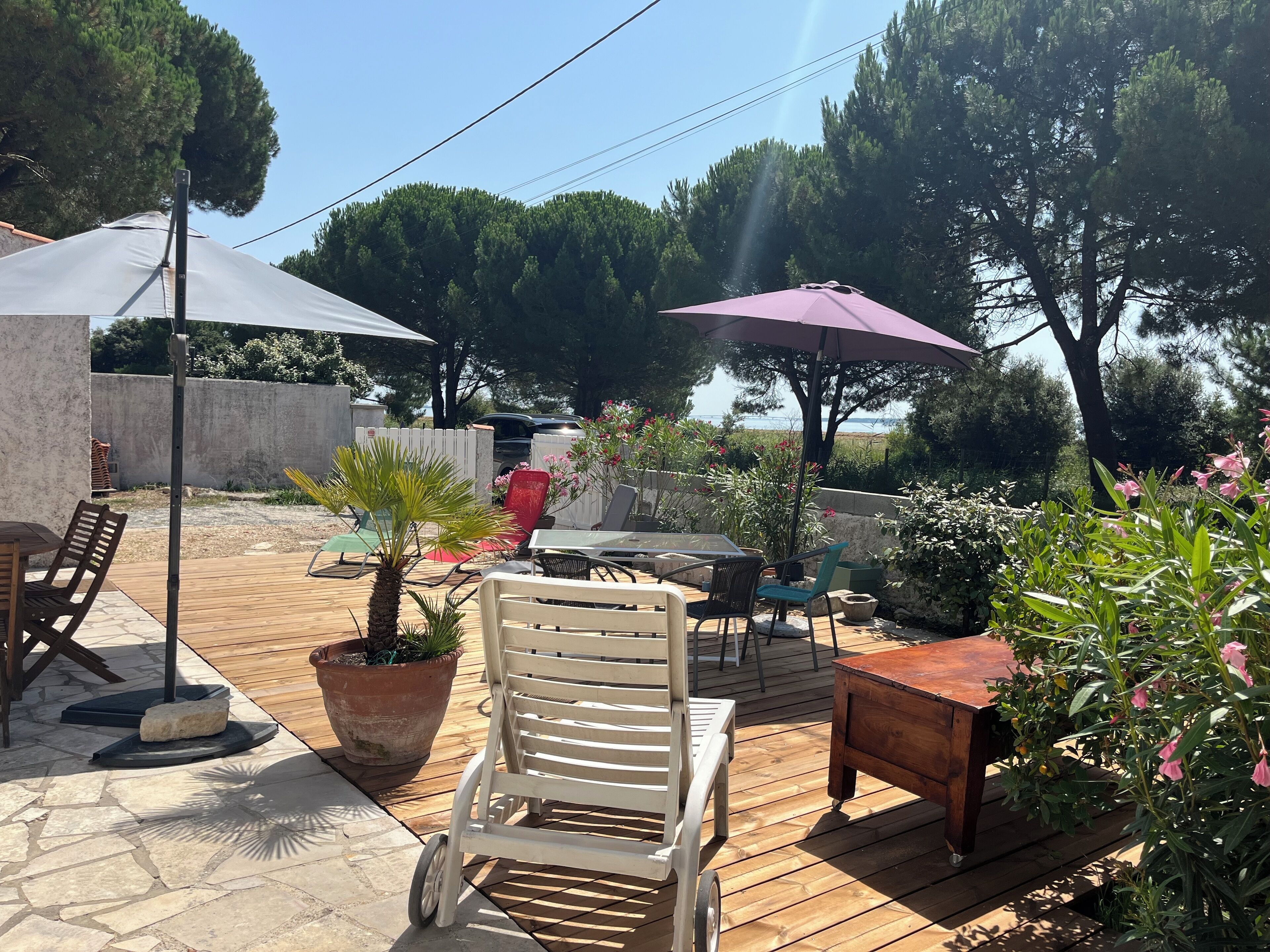 An outdoor patio with a wooden deck, a table, chairs, and umbrellas.