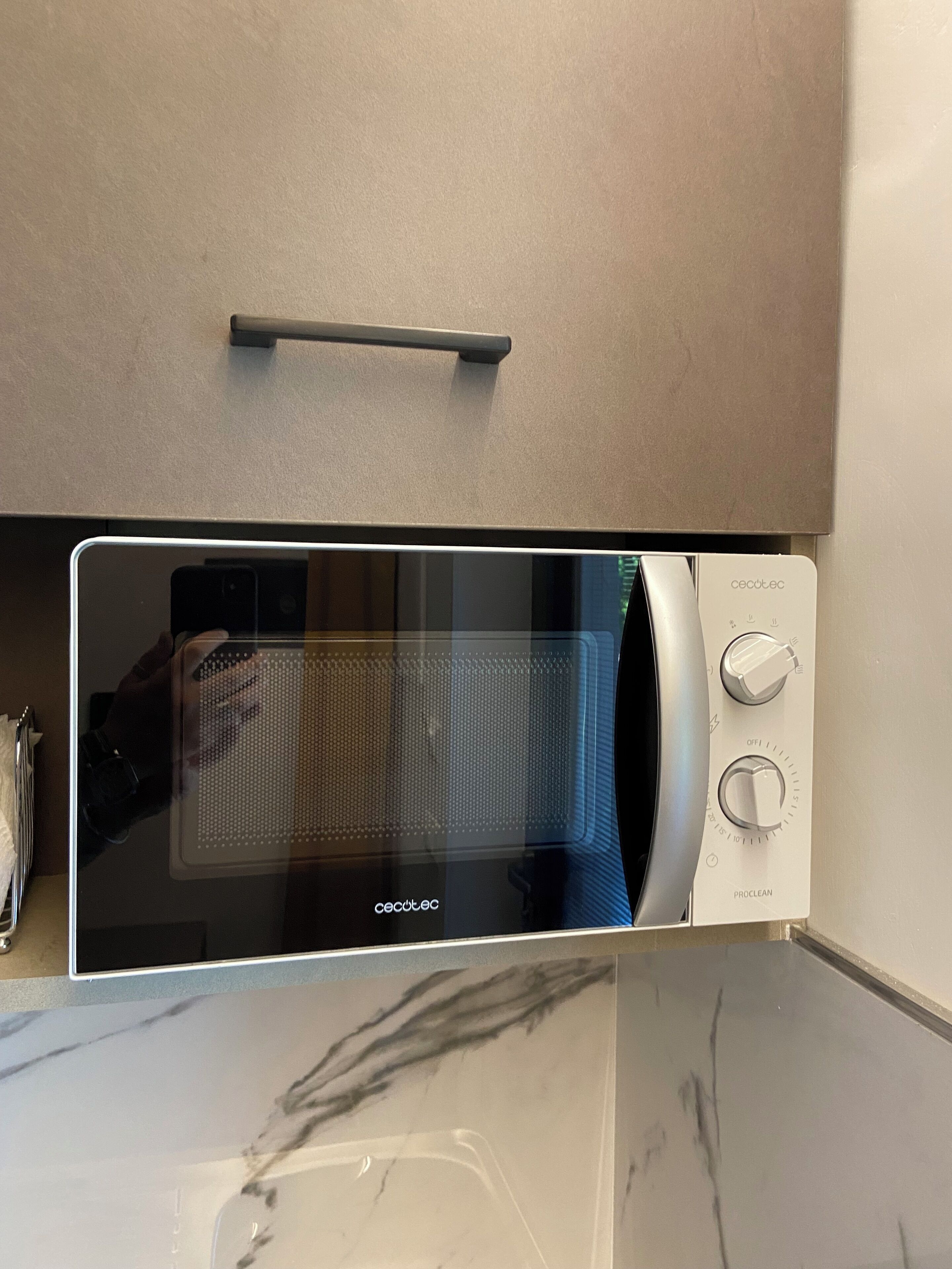 A modern kitchen with a built-in microwave, a handle above it, and a marble countertop.