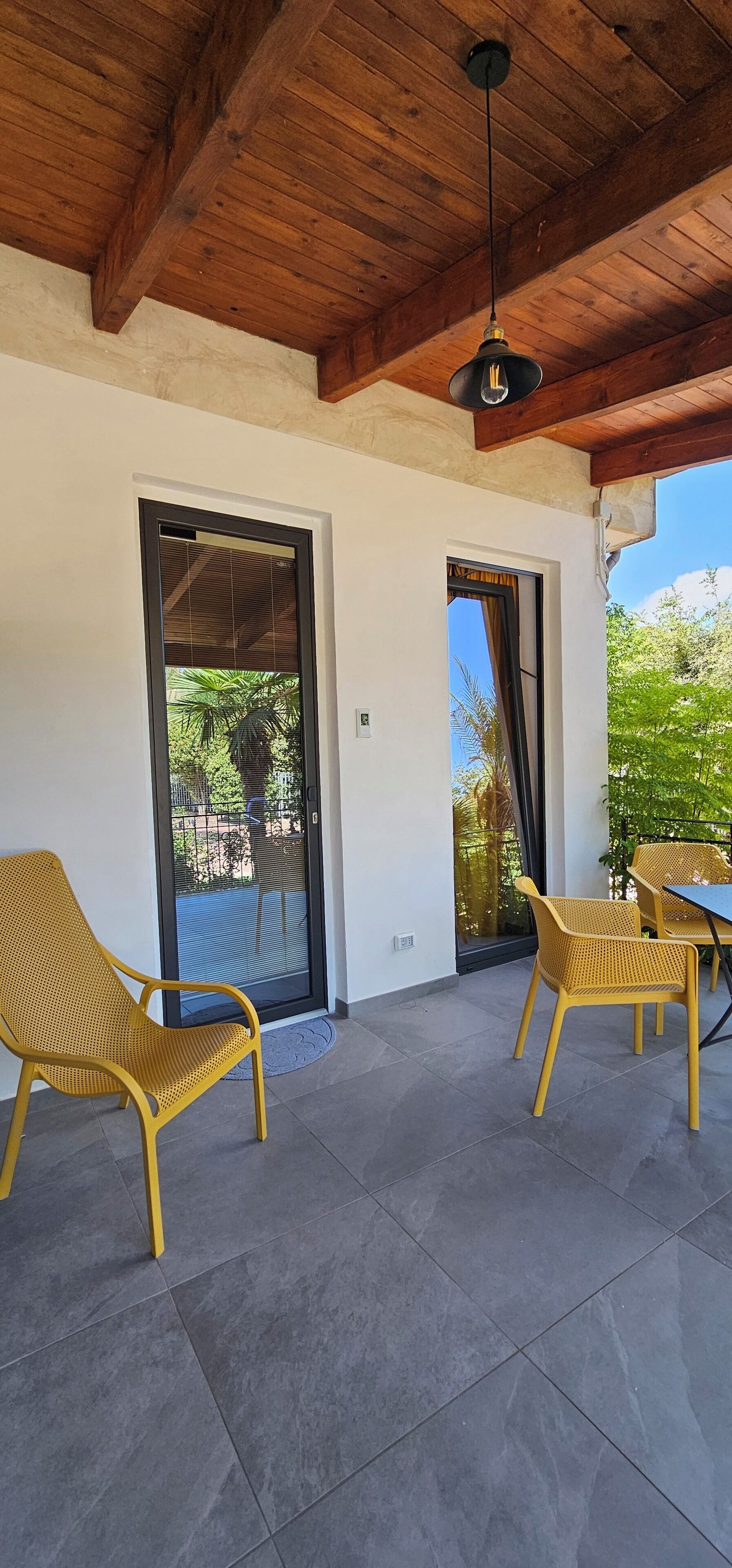 Un'area patio coperta con due poltrone gialle in vimini, un tavolo e una ventola a soffitto.
