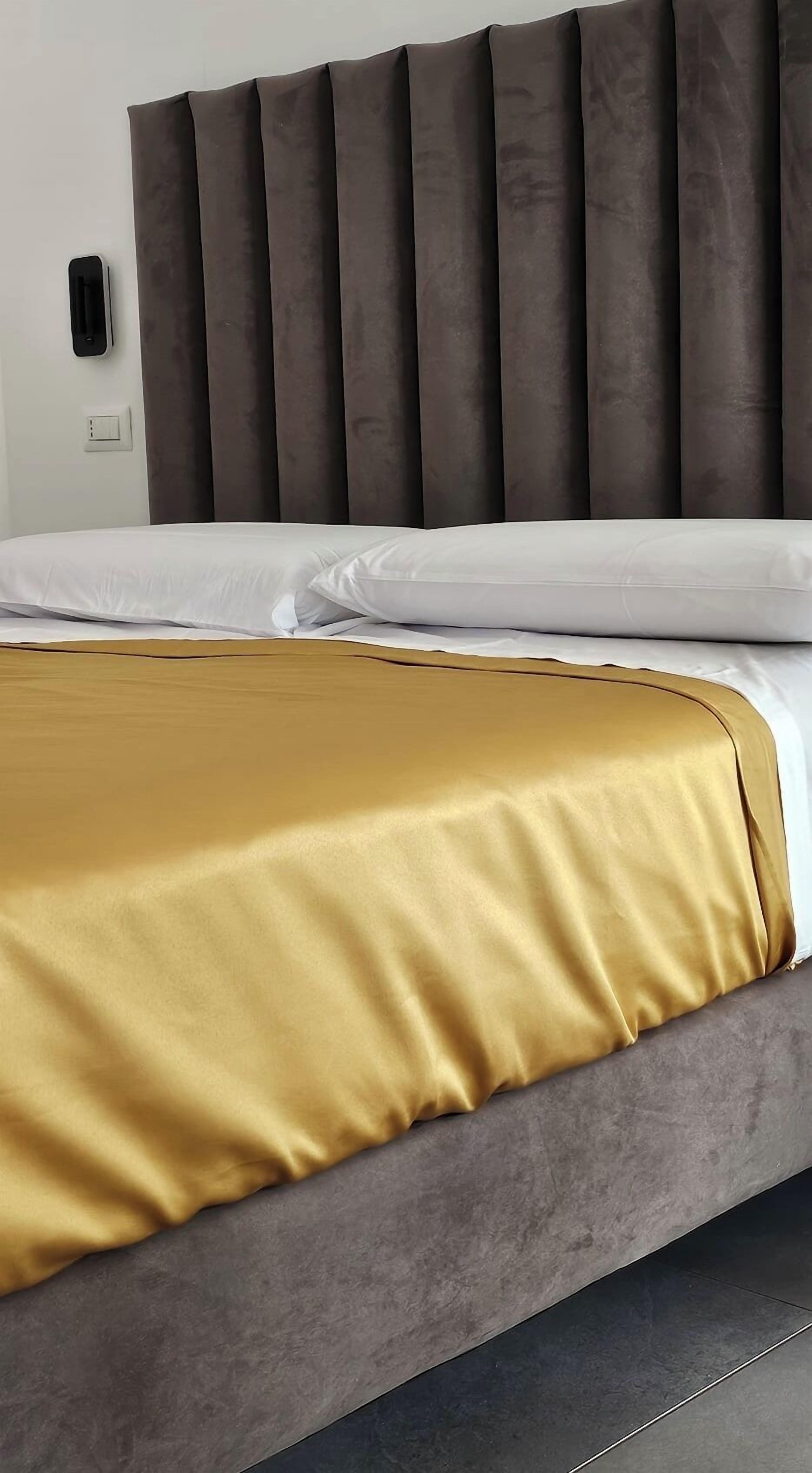 A bed with a gold-colored bedspread and a grey upholstered headboard.