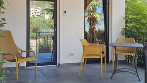 Ein überdachter Patio-Bereich mit zwei Korbstühlen und einem Tisch, einer Holzbalkendecke und Blick durch eine Glastür ins Freie.