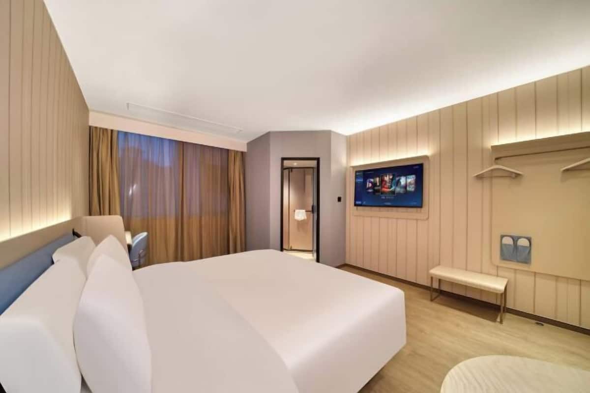 Une chambre d’hôtel avec un grand lit, une télévision, un banc et un miroir.