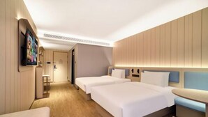 Une chambre d’hôtel moderne avec deux lits, une petite table et un téléviseur fixé au mur.