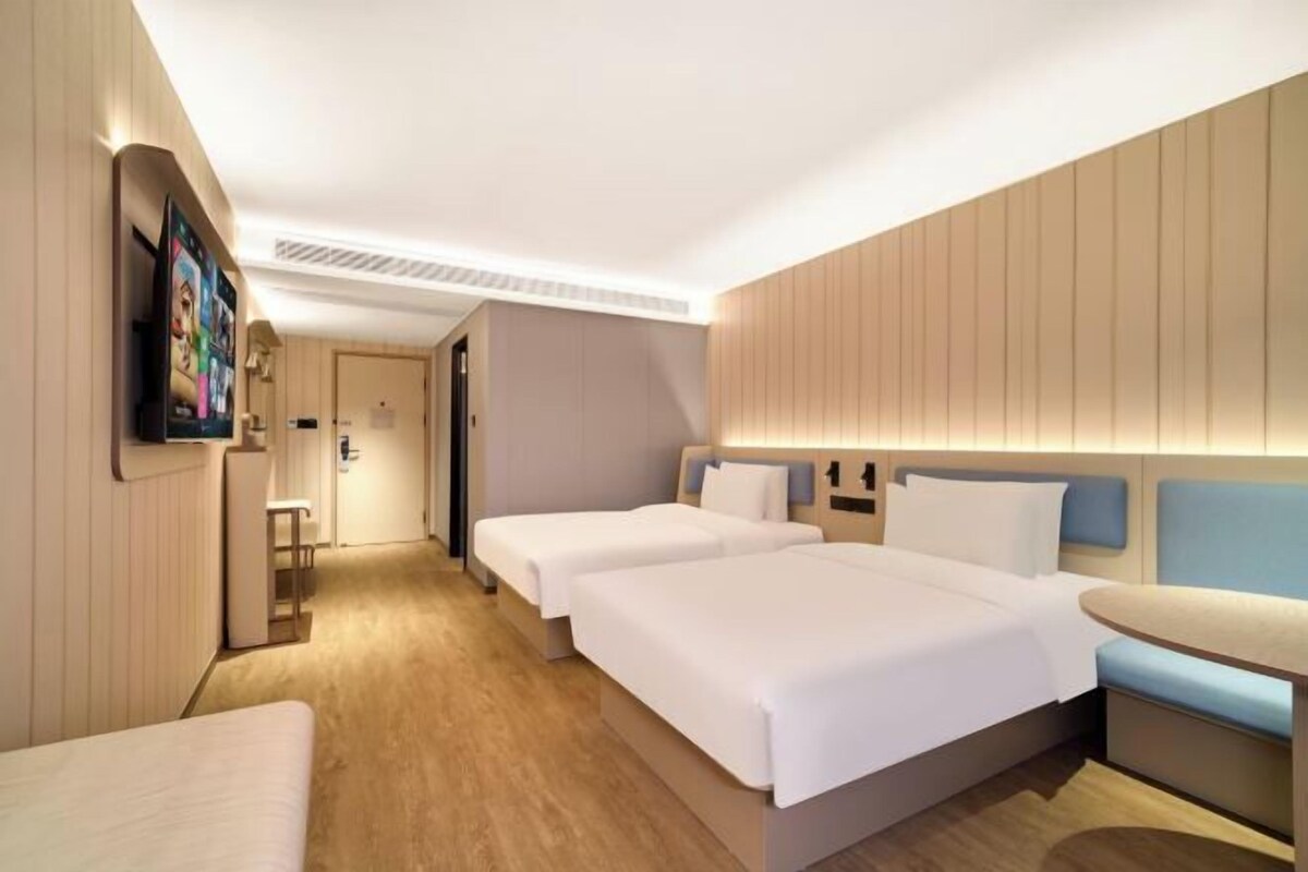 Une chambre d’hôtel moderne avec deux lits, une petite table et un téléviseur fixé au mur.