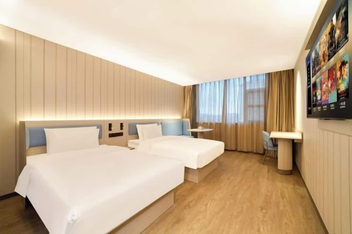 Une chambre d’hôtel avec deux lits, un bureau, une chaise et un téléviseur fixé au mur.