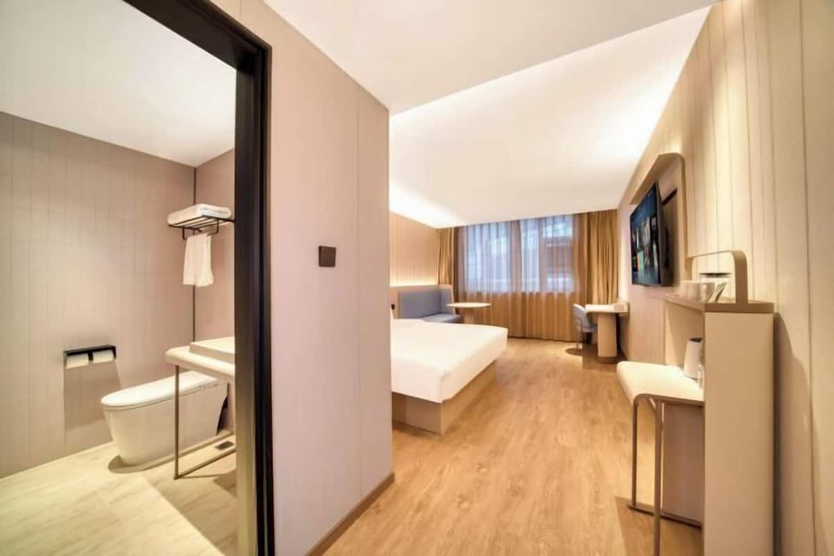 Une chambre d’hôtel moderne avec un plancher en bois, un lit, un bureau et une salle de bain équipée de toilettes et d’un lavabo.