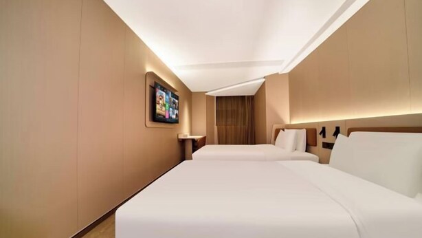 Une chambre d’hôtel avec deux lits, un téléviseur à écran plat fixé au mur et un plancher en bois.