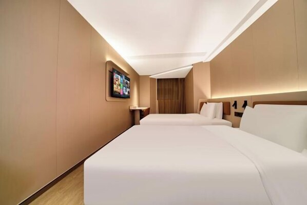 Une chambre d’hôtel avec deux lits, un téléviseur à écran plat fixé au mur et un plancher en bois.