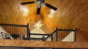 Un'ampia sala da pranzo con soffitto alto e travi in legno, caratterizzata da una scalinata centrale e una ventola a soffitto.
