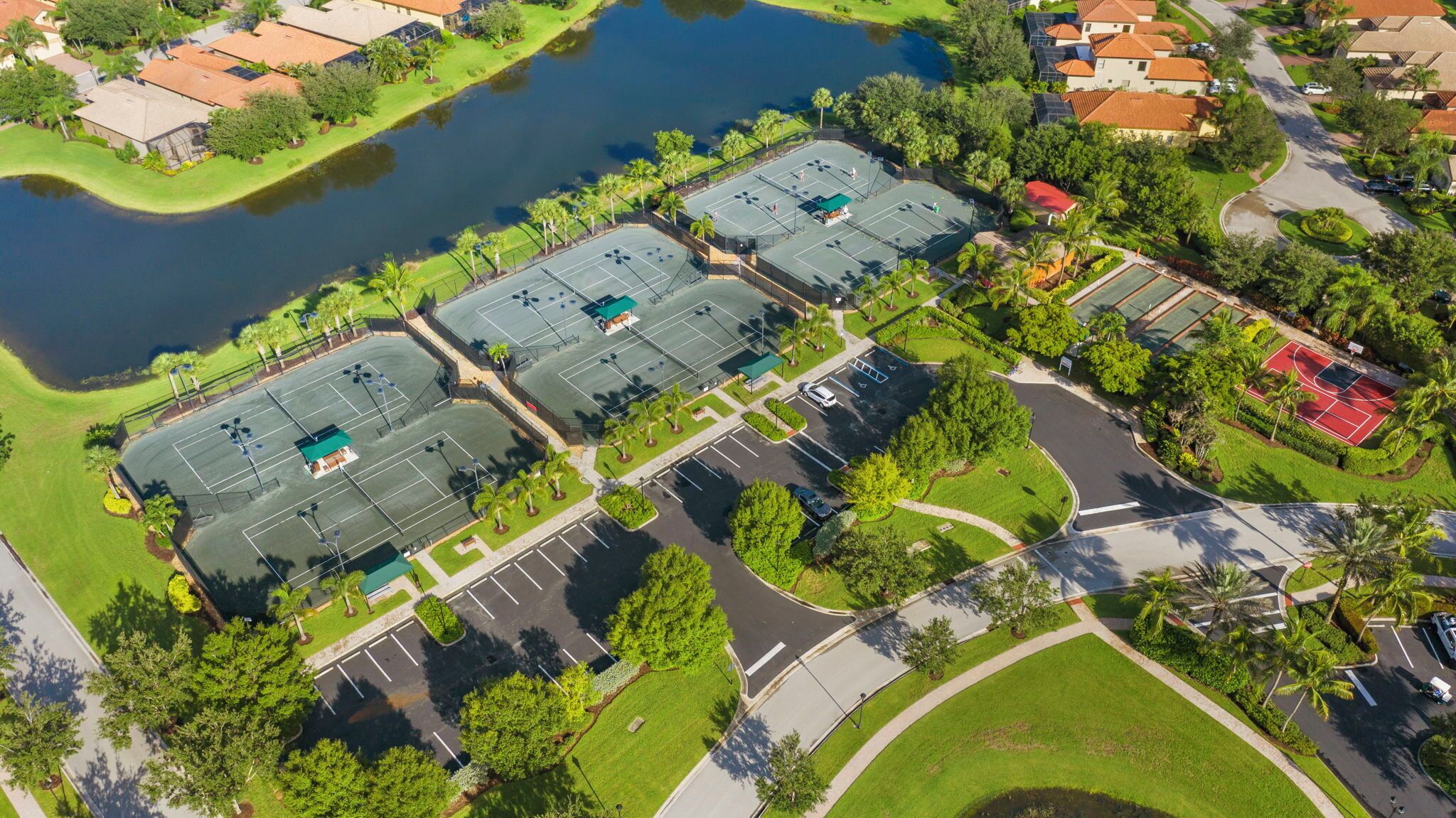 Vue aérienne d’un quartier résidentiel avec plusieurs courts de tennis, un petit étang et de la végétation luxuriante tout autour.