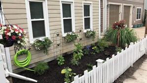 A residential house with a white picket fence, a garden with various plants, and hanging flower baskets.