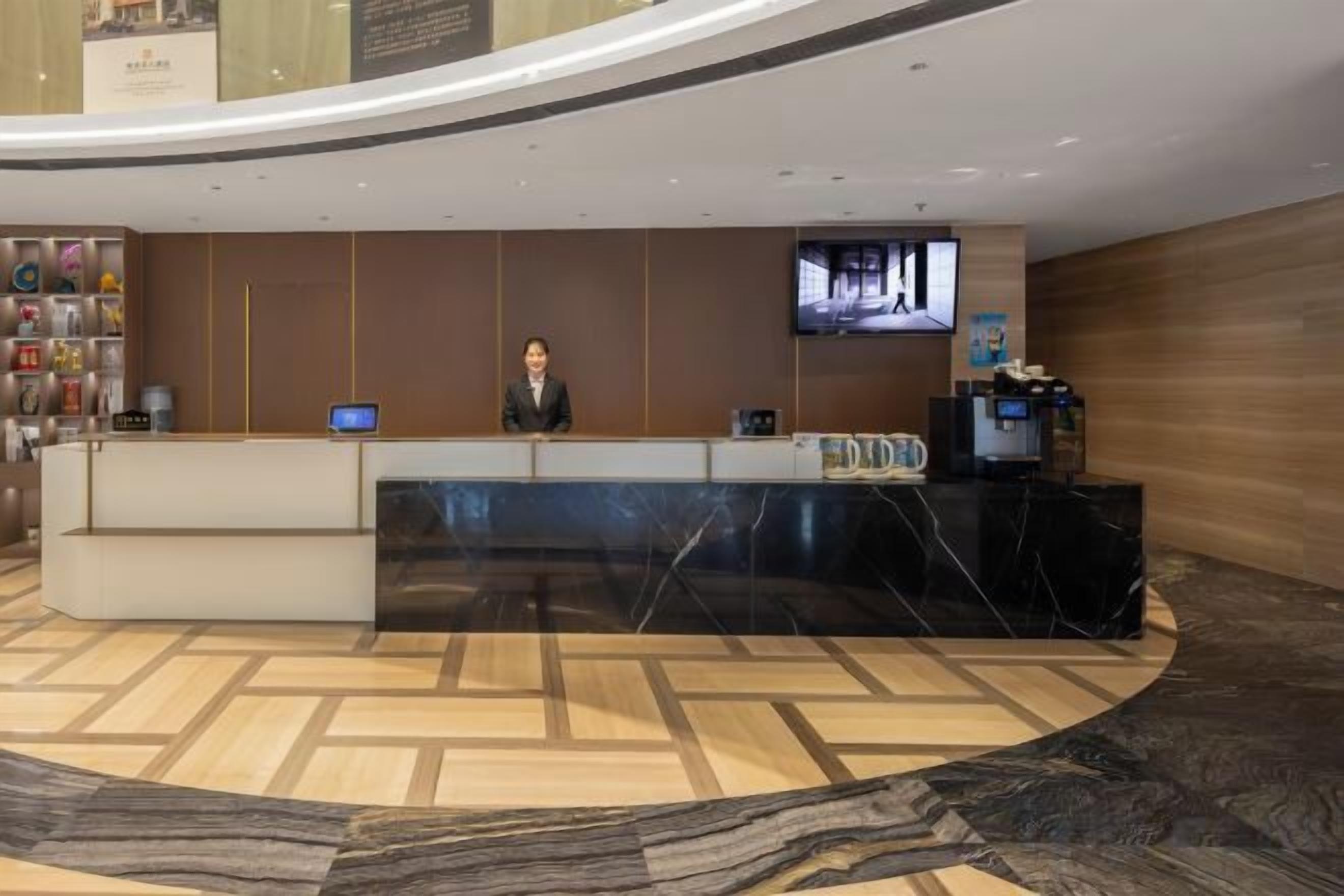 A hotel reception area with a marble reception desk, a flat-screen TV, and a digital display.