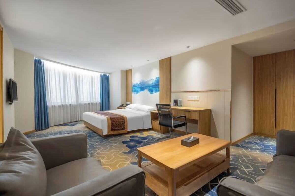 A hotel room with a bed, a desk, a chair, a sofa, and a television.
