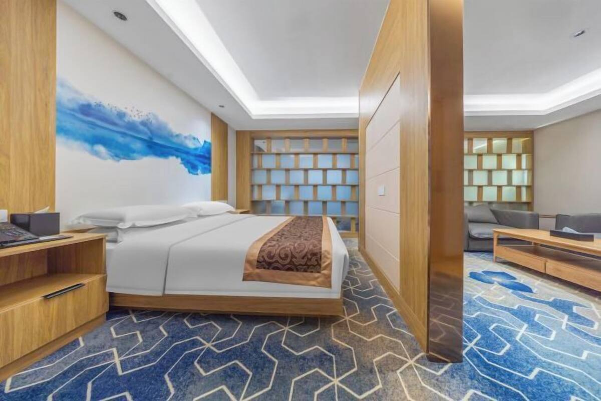 A modern hotel room with a bed, a desk, a chair, a sofa, and a wall with a geometric pattern.