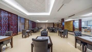 A hotel conference room with multiple tables and chairs, a large window, and a decorative wall.