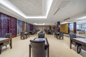 Uma sala de conferências de hotel com várias mesas e cadeiras, uma janela grande e um painel decorativo.
