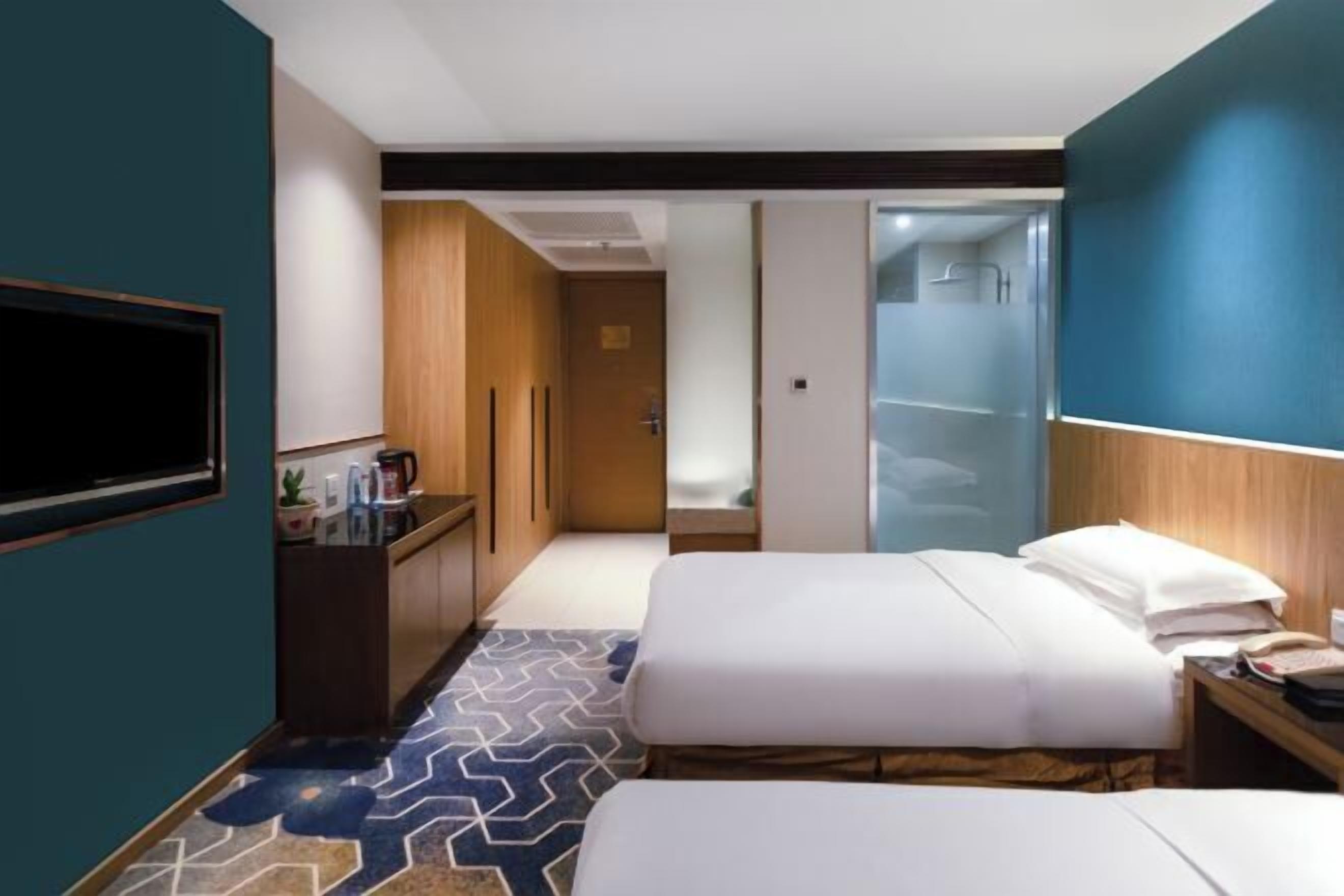 A hotel room with two beds, a desk, a TV, and a bathroom with a glass shower.