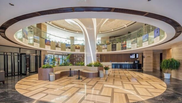 Un hall amplio con una zona de estar central, un mostrador de recepción y un atrio de cristal con luz natural.