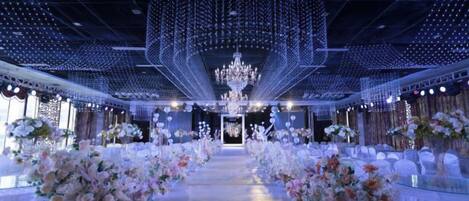 An indoor venue with a central aisle, chandeliers, and floral arrangements.