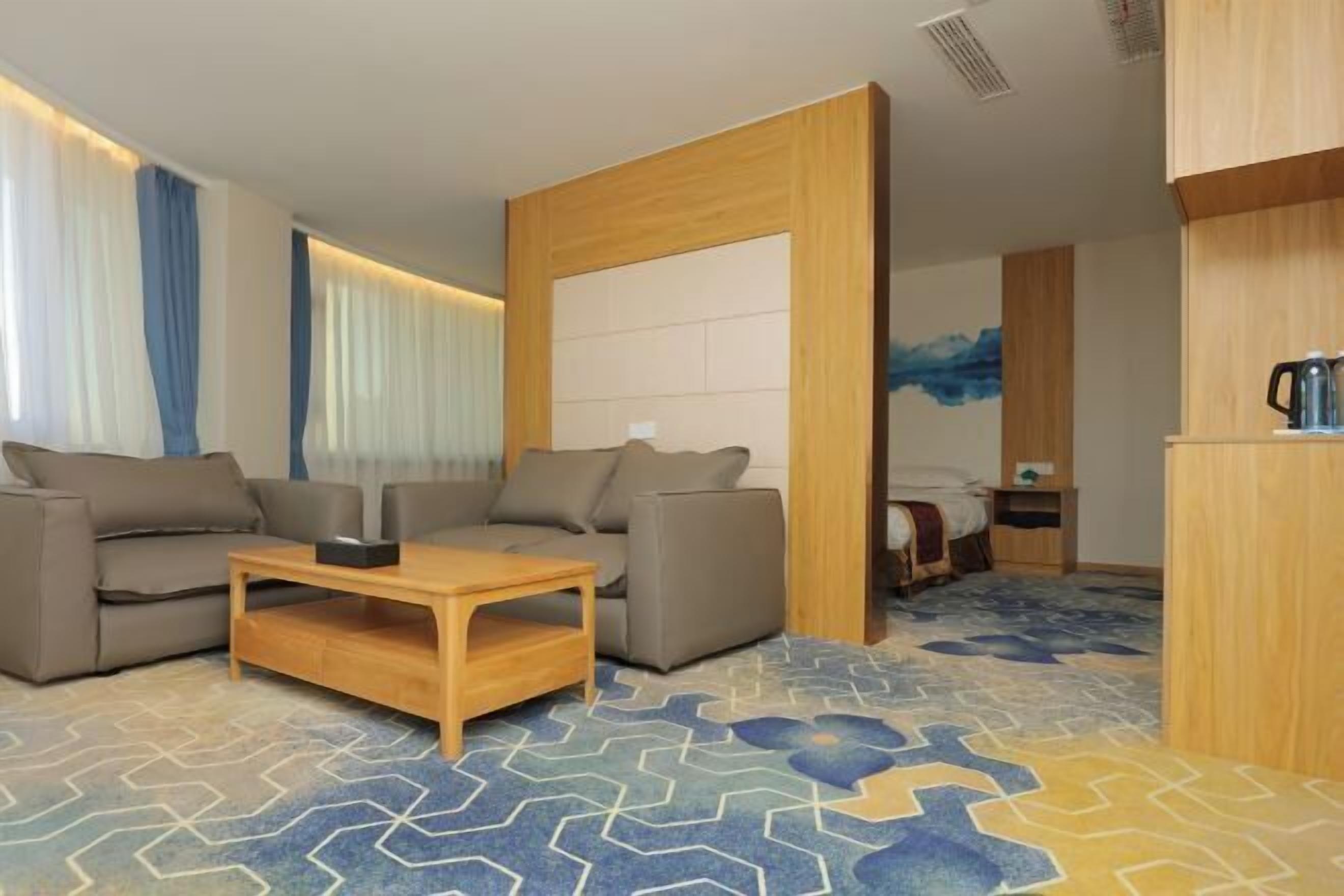Una habitación de hotel moderna con un conjunto de sofá, una mesa de centro de madera y una alfombra estampada.