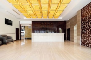 A spacious lobby with a modern reception desk, a patterned wall, and a flat-screen TV mounted on the wall.